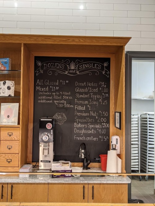 Chalkboard menu displaying prices for donuts, including glazed, filled, and specialty options, in a cozy cafe setting.
