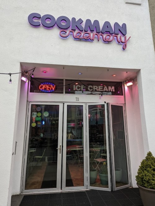 Entrance of Cookman Creamery with a bright "OPEN" sign and colorful ice cream branding.