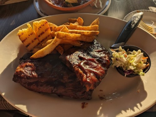 A plate featuring grilled ribs, seasoned fries, and a side of coleslaw.