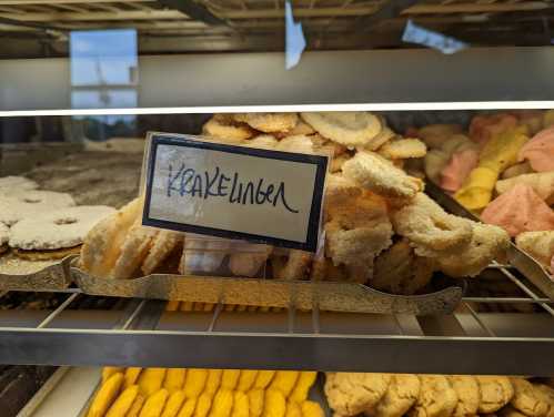 A display case filled with various baked goods, featuring a sign labeled "Krakelber."