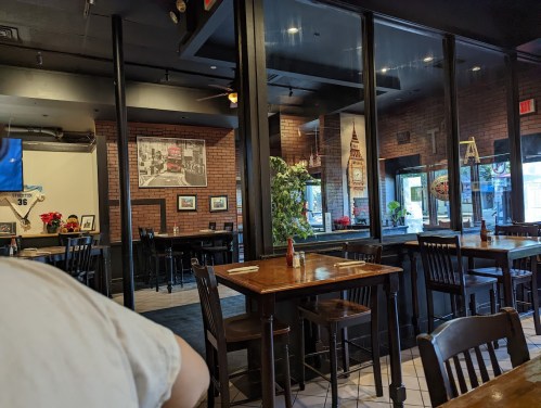 Interior of a restaurant featuring wooden tables, black chairs, and brick walls with decor and plants.