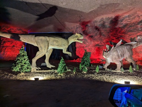Two dinosaur sculptures in a dimly lit cave, surrounded by small trees and red lighting.