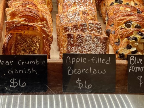 A display of pastries including pear crumble danish, apple-filled bear claw, and blueberry almond croissant with prices.