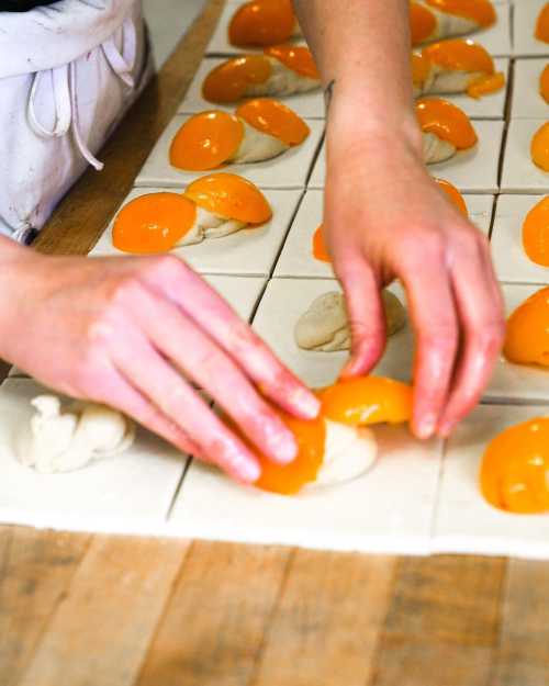 A person placing orange fruit slices onto squares of dough on a wooden surface.