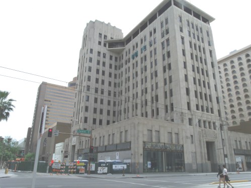 A tall, historic building with a unique architectural design, located at a city intersection, surrounded by modern structures.