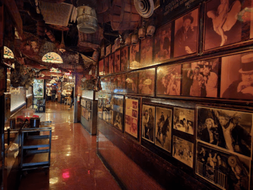A dimly lit hallway lined with vintage photographs and memorabilia, leading to a lively bar area.