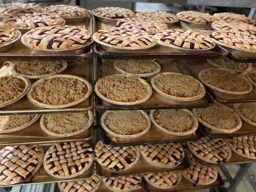 A display of various pies, including lattice-topped and crumb-topped varieties, stacked on trays.