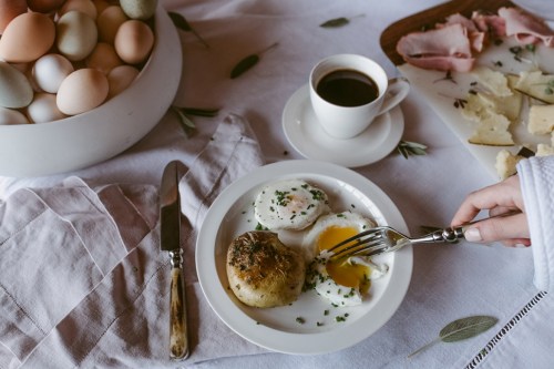 A plate with poached eggs and a savory muffin, alongside a cup of coffee and a bowl of colorful eggs.