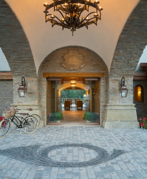 A stone archway entrance with a chandelier, lanterns, and a bicycle parked outside on cobblestone.