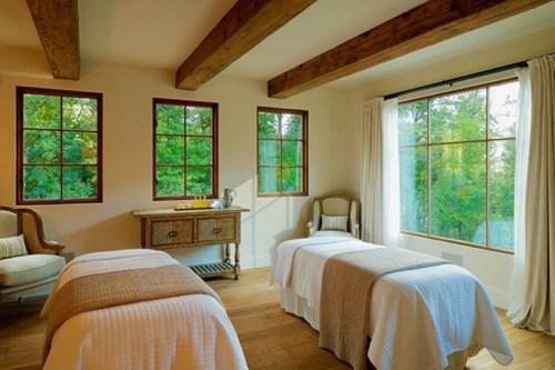 A serene bedroom with two twin beds, large windows, and natural light, featuring wooden beams and a cozy atmosphere.