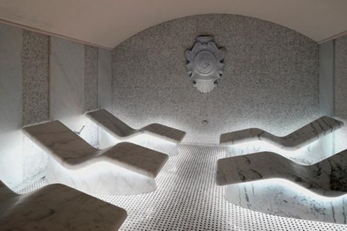 A serene spa room with marble lounge chairs and soft lighting, featuring a decorative wall emblem.