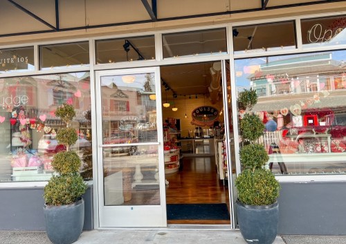 A storefront with large glass doors, decorated with hearts, showcasing a sweet shop interior.