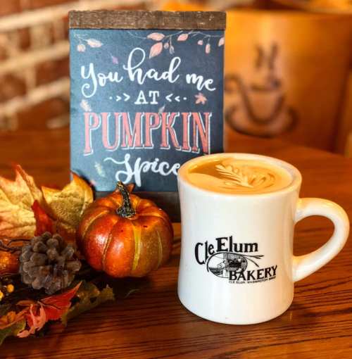A cozy scene featuring a pumpkin spice latte, a small pumpkin, and a decorative sign on a wooden table.
