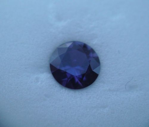 A round, faceted purple gemstone resting on a light-colored surface.