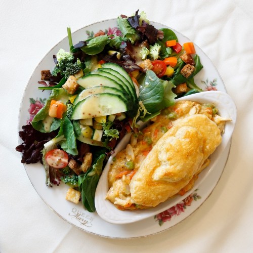 A plate featuring a creamy chicken dish with a side salad of mixed greens, cucumbers, and colorful vegetables.