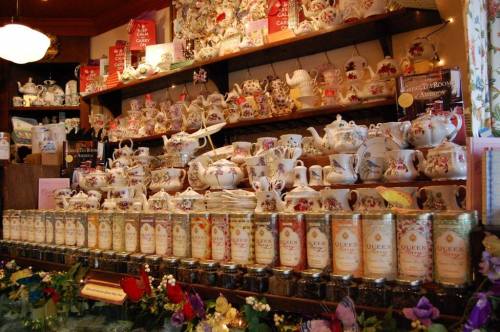A display of colorful teapots, cups, and jars of tea on shelves, adorned with floral decorations.
