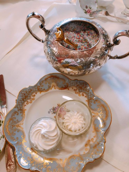 A silver sugar bowl with a floral design beside a plate holding two small meringue desserts.