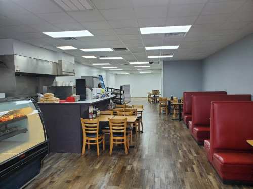 Interior of a restaurant featuring booths, tables, and a display case, with a clean, modern design and bright lighting.