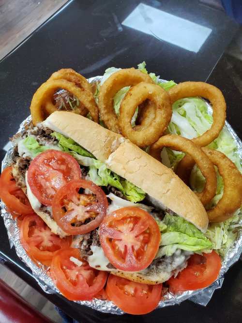 A large sandwich with lettuce, tomatoes, and meat, served with onion rings and a side of lettuce on a silver platter.