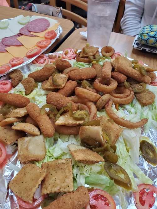 A large platter of assorted fried foods, including onion rings, jalapeños, and breaded items, served on lettuce and tomatoes.