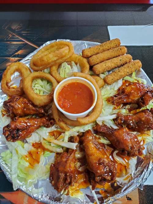 A platter of chicken wings with sauce, onion rings, mozzarella sticks, and marinara sauce on a bed of lettuce.