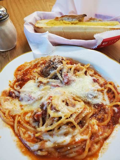 A plate of spaghetti with meatballs and marinara sauce, topped with cheese, alongside a basket of garlic bread.