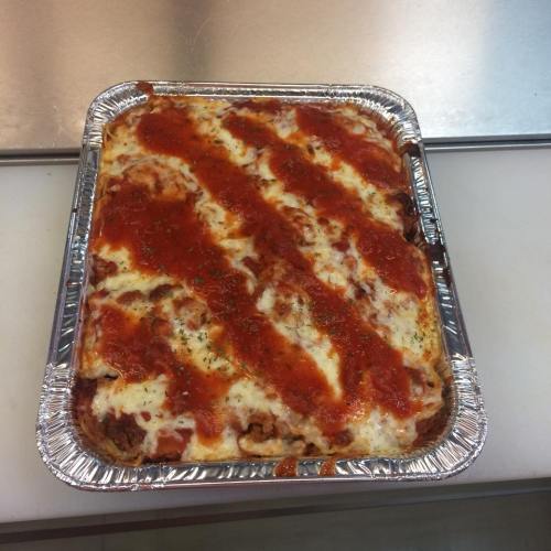 A rectangular aluminum tray filled with baked lasagna topped with marinara sauce and melted cheese.
