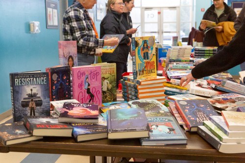 A table filled with various books, with people browsing in a colorful room.