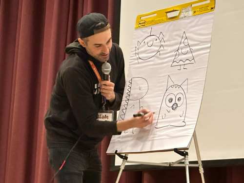 A person draws simple cartoon characters on a large flip chart during a presentation.