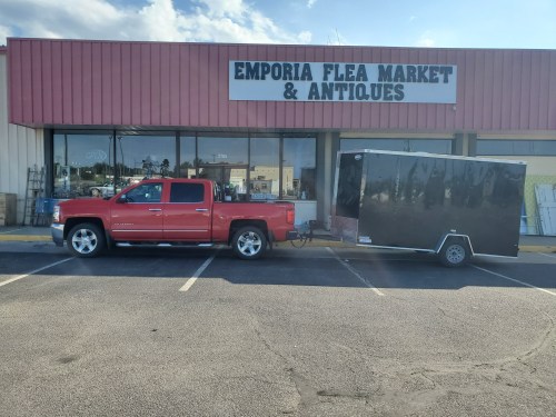 A red pickup truck parked next to a black trailer in front of the Emporia Flea Market & Antiques building.