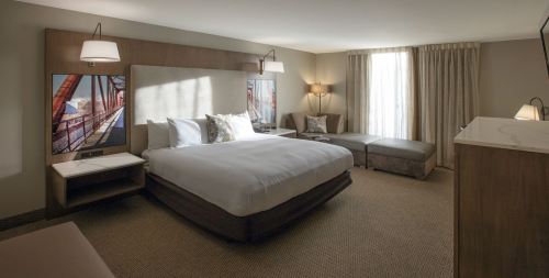 A modern hotel room featuring a king-sized bed, seating area, and large window with natural light.