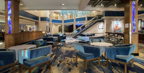 Modern hotel lobby featuring blue velvet seating, a staircase, and colorful artwork on the walls.