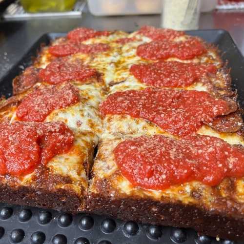 A close-up of a rectangular pizza topped with melted cheese and dollops of marinara sauce, on a black tray.