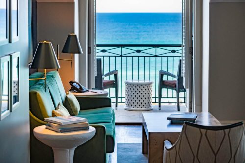 Cozy living area with a green sofa, coffee table, and ocean view from a balcony. Bright and inviting atmosphere.