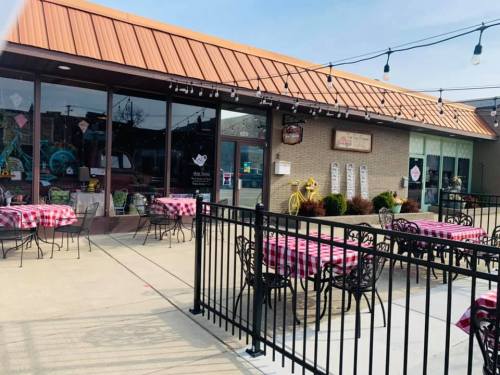 A charming restaurant with outdoor seating, featuring checkered tablecloths and a welcoming facade under a blue sky.