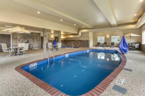 Indoor swimming pool with blue water, surrounded by lounge chairs and umbrellas, in a well-lit, modern space.