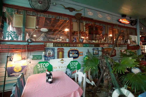 A cozy restaurant interior with vintage signs, a checkered tablecloth, and tropical plants.