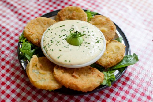 A plate of crispy fried green tomatoes arranged around a bowl of creamy dipping sauce, garnished with herbs.