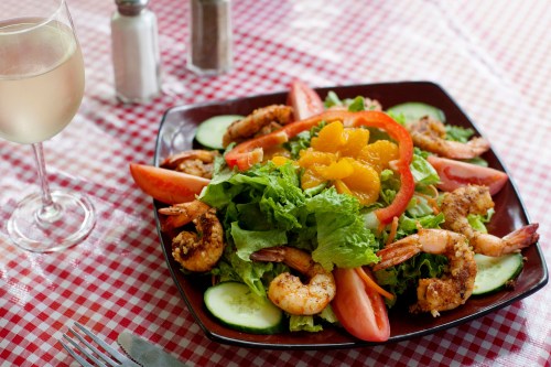 A vibrant salad with shrimp, tomatoes, cucumbers, and orange slices, served with a glass of white wine.