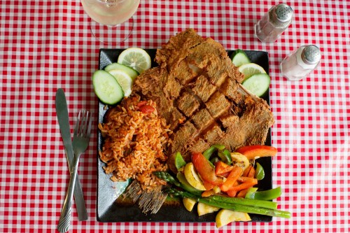 A plate of fried meat with rice, sautéed vegetables, and cucumber slices, set on a red checkered tablecloth.