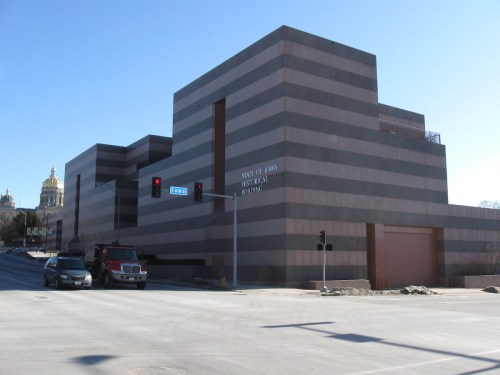 Modern building with striped brown exterior, labeled "State of Iowa Historical Building," near traffic lights and a road.