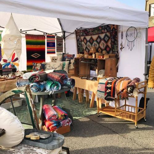 A vibrant market stall displaying colorful textiles, blankets, and handmade crafts under a white tent.