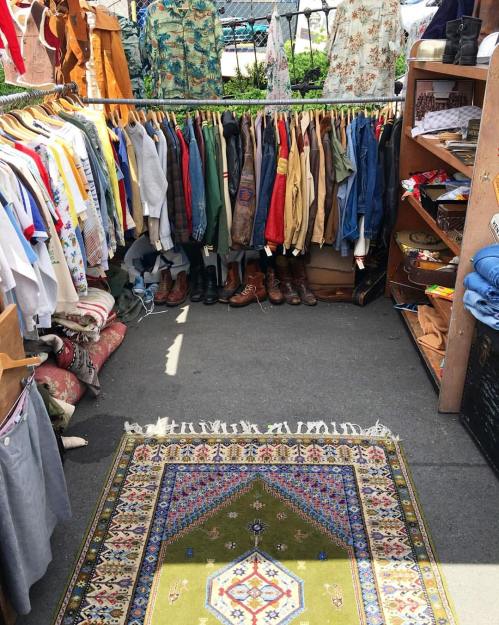 A vibrant market stall displaying a variety of clothing on hangers and a patterned rug on the ground.