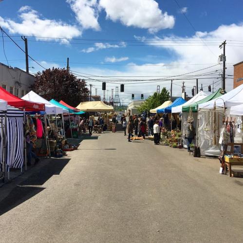 A vibrant outdoor market with colorful tents lining a street, under a blue sky with scattered clouds.