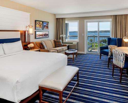 A bright hotel room featuring a king bed, seating area, and large windows with a view of the water.