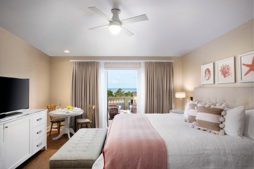 Cozy hotel room with a king bed, seating area, and balcony view of the ocean. Light colors and modern decor.