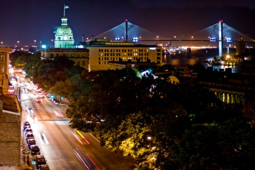 Night view of a cityscape featuring a bridge, waterfront, and historic buildings illuminated by streetlights.