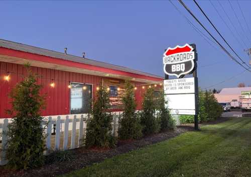 Exterior of Backroads BBQ restaurant at dusk, featuring a sign and decorative greenery.