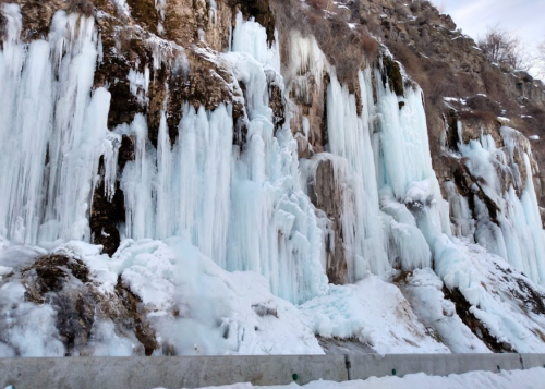 Icicles and frozen waterfalls cascade down a rocky cliff, surrounded by snow and ice.