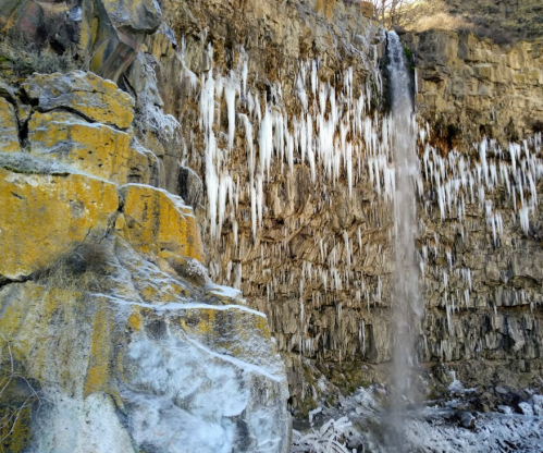 A frozen waterfall cascading down a rocky cliff, surrounded by icicles and snow-covered rocks.